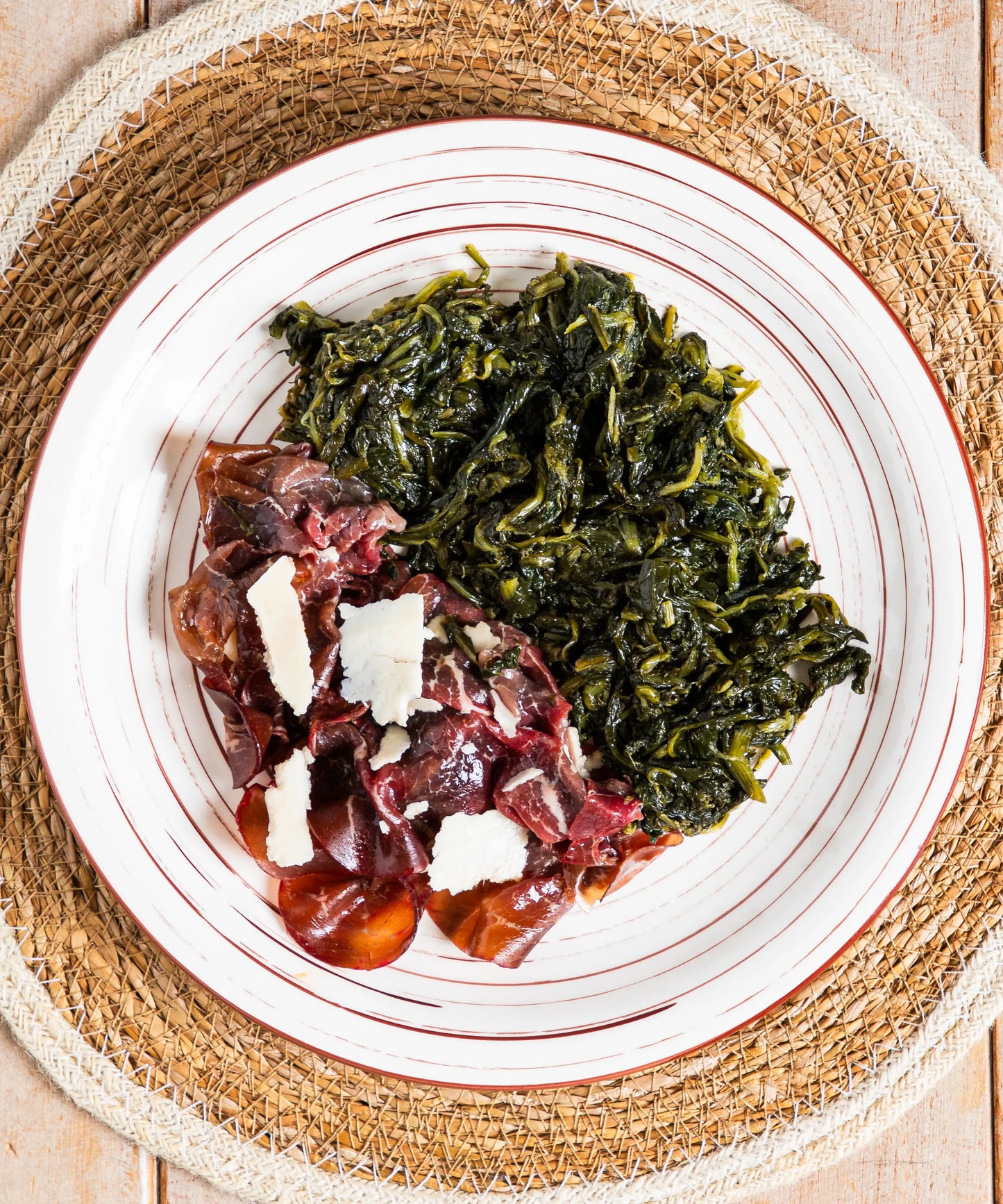Piatto di ceramica bianca con strisce rosse contenente bresaola della valtellina igt con grana dop e cicorietta ripassata dal gusto autentico