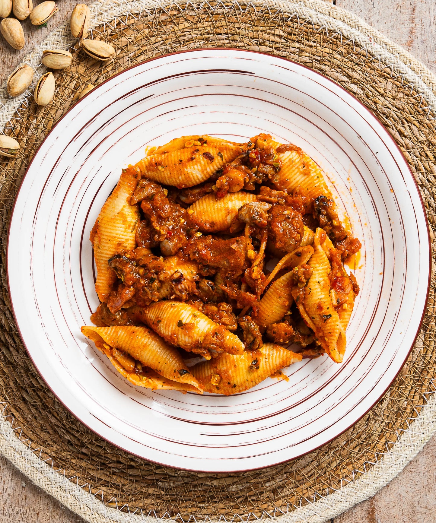 Un piatto di conchiglioni in salsa ragù di mare con pistacchi servito su piatto bianco con strisce marroni concentriche