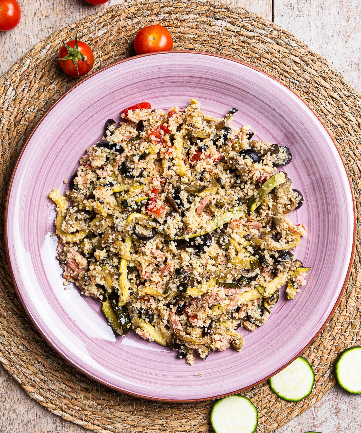 Cous cous con verdure grigliate e tonno servito su un piatto rosa in ceramica con quinoa e olive nere