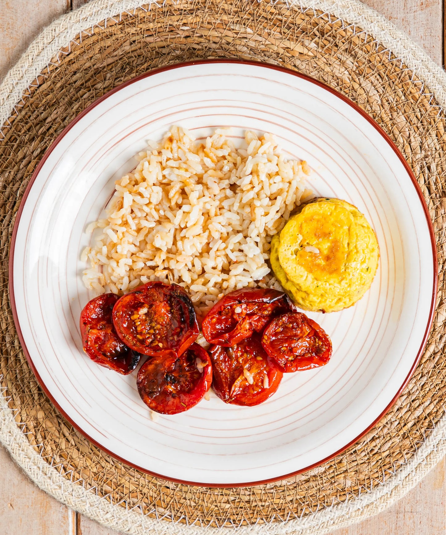 Piatto in ceramica bianca con bordo rosso contenente frittatina alle verdure con riso e pomodorini arrosto