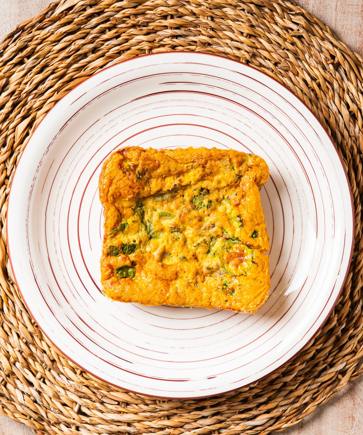 Frittatina di mare e zucchine dorata servita su piatto bianco con strisce rosse, ideale con salsiccia e zuppa di lenticchie