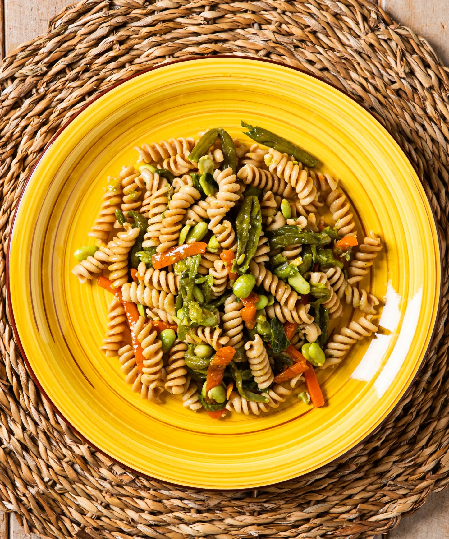Fusilli integrali con verdure ed edamame su piatto giallo con risalto per zuppa lenticchie e salsiccia