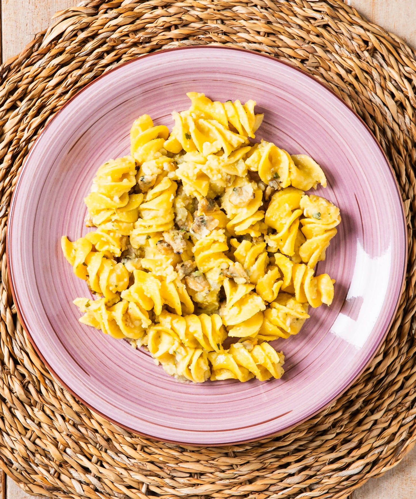 Piatto cremoso di fusilloni in crema di patate e vongole su piatto rosa in ceramica con grano duro