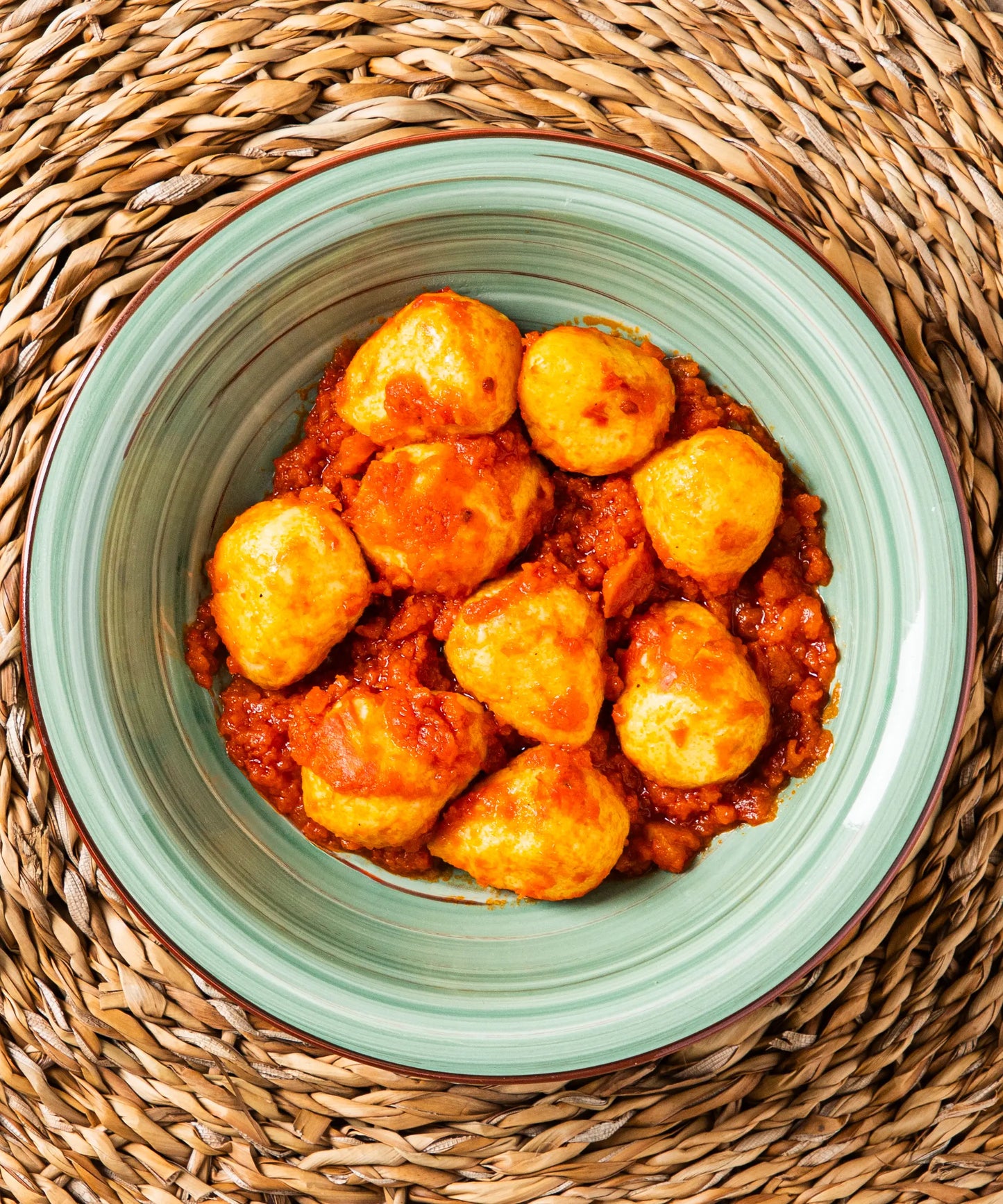 Ciotola verde chiaro in ceramica con bordo marrone contenente gnocchi di patate ripieni di salsiccia in sugo al pomodoro per un pasto completo dal gusto tradizionale