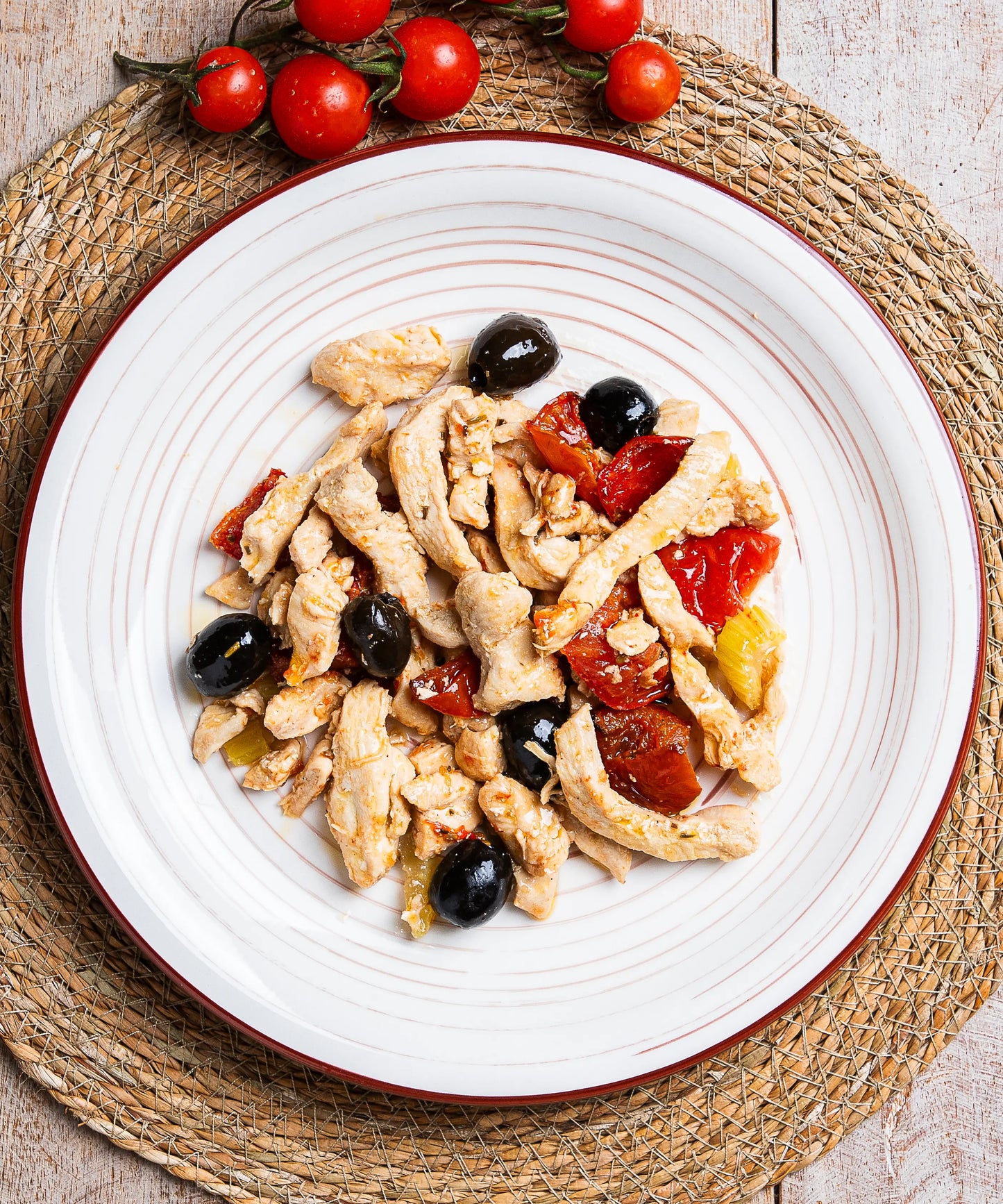 Insalata di pollo verdure e olive con strisce di pollo cotto, olive nere e pomodori arrosto su piatto ceramica bianco con bordo rosso