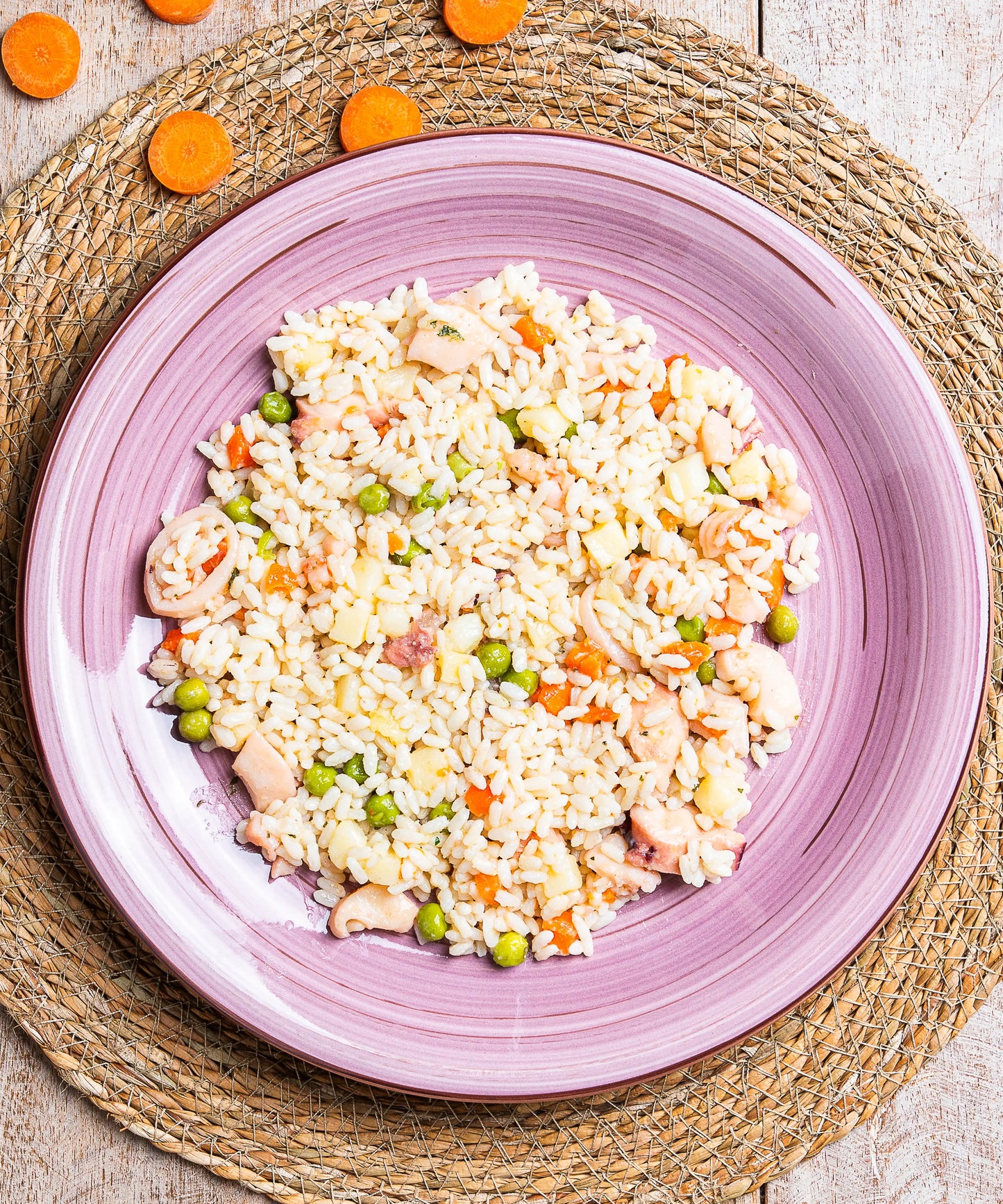 Una vivace insalata di riso al profumo di mare con polpo gamberi e seppie servita su un piatto ceramico viola con scanalature concentriche