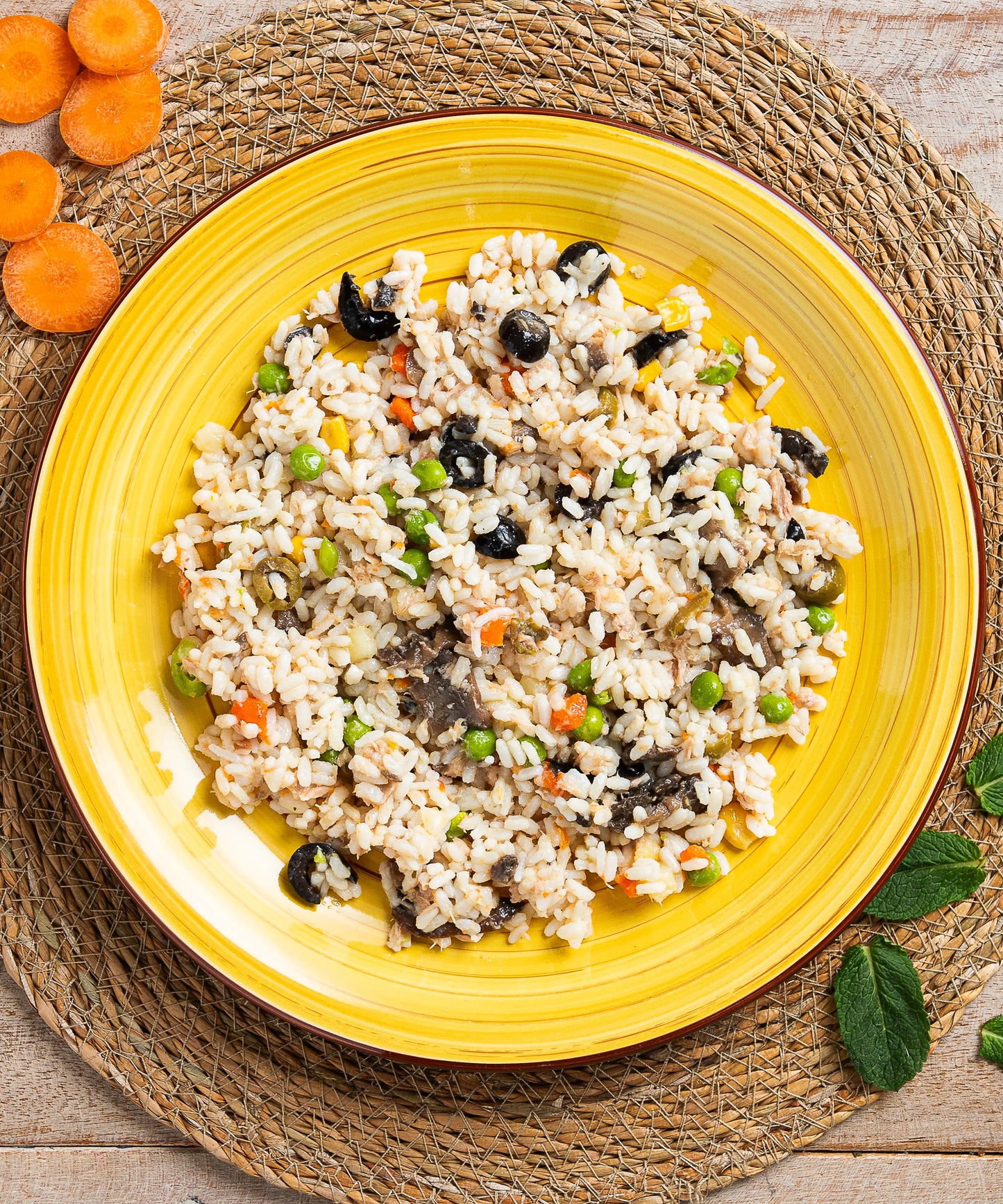 Una vivace insalata di riso classica con riso integrale, piselli verdi, carote e olive scure su piatto giallo ceramico