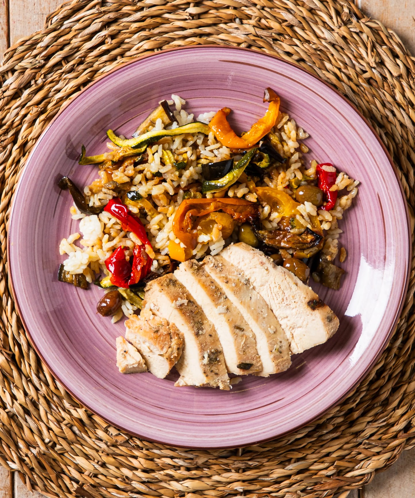 Piatto in ceramica lavanda con tagliata di pollo, riso carnaroli, verdure colorate e olive taggiasche per un pasto sano