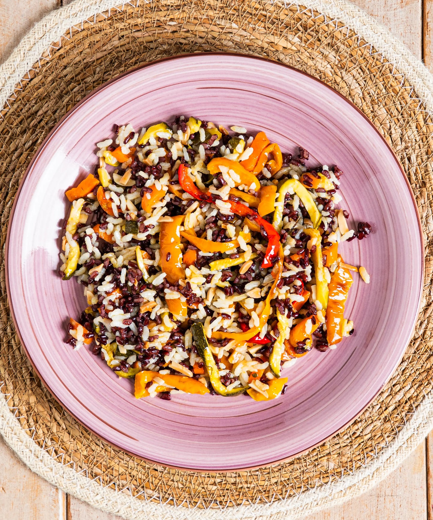 Vibrante insalata di riso vegan con mandorle peperoni zucchine in ciotola rosa per piatti senza salsiccia o lenticchie