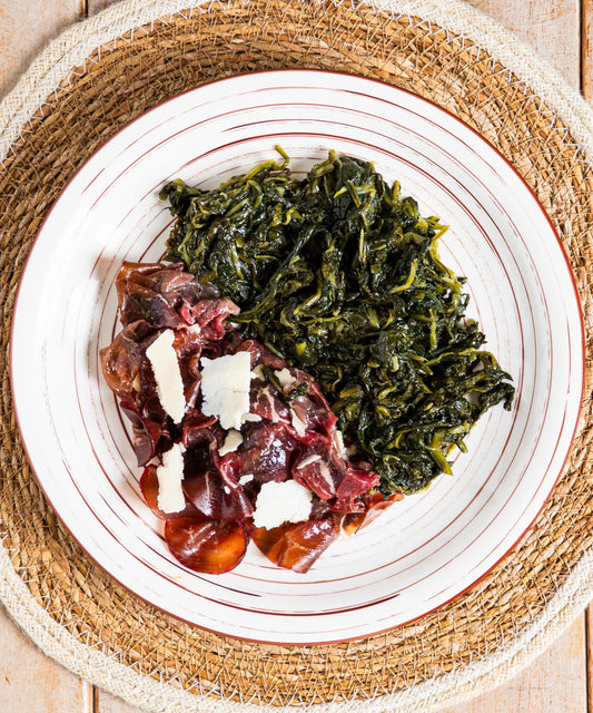Piatto di ceramica bianca con strisce rosse contenente bresaola della valtellina igt con grana dop e cicorietta ripassata dal gusto autentico