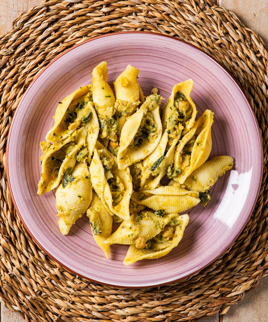Una piatto di conchiglioni al pesto di zucchine e ceci con gusto delicato servito su piatto rosa in ceramica