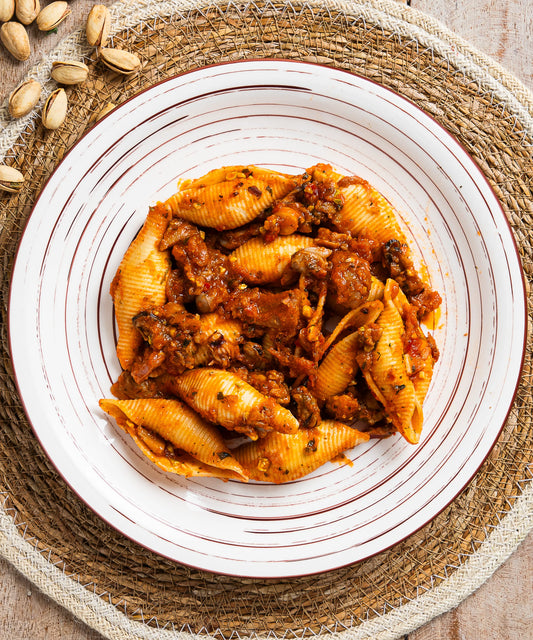 Un piatto di conchiglioni in salsa ragù di mare con pistacchi servito su piatto bianco con strisce marroni concentriche