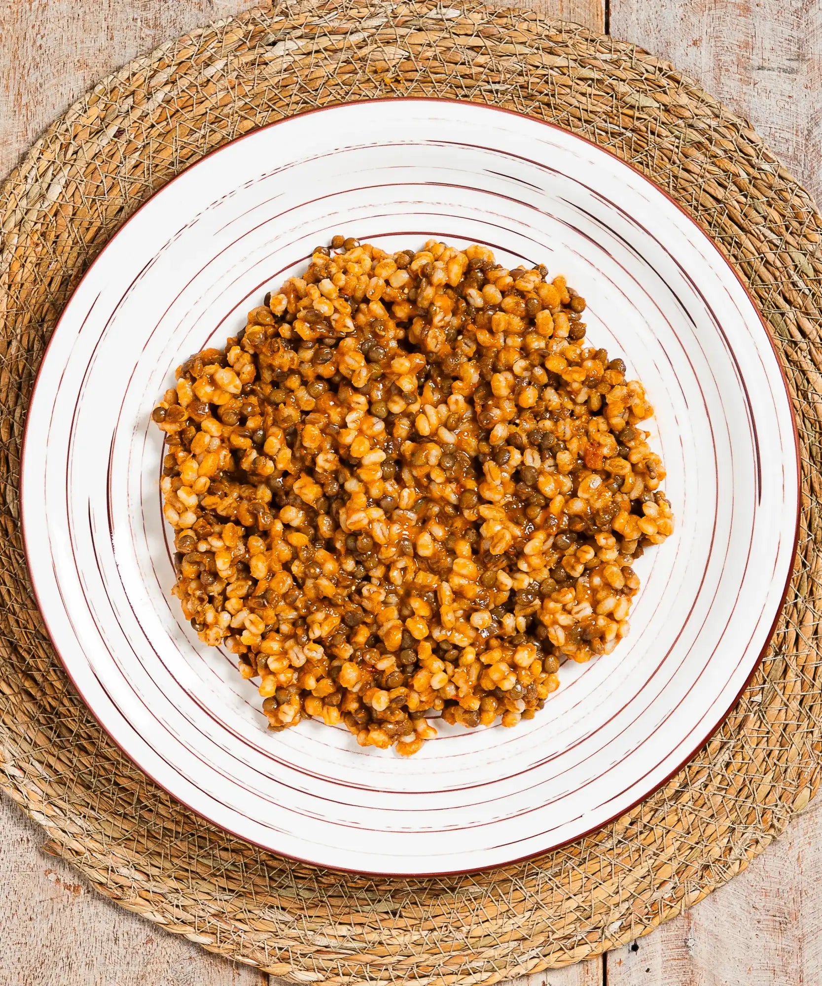 Un cumulo di lenticchie e grani dorati-brunastri e lucidi servito su un piatto bianco con sottili anelli concentrici marroni.