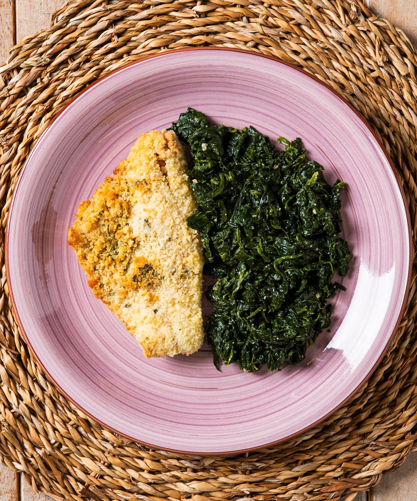 Piatto rosa in ceramica con filetto di branzino gratinato dorato e spinaci saltati dal gusto raffinato