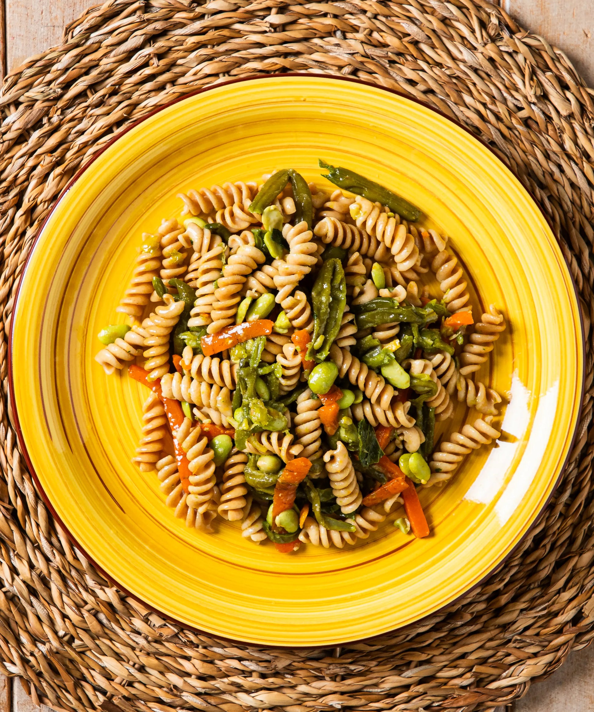 Fusilli integrali con verdure ed edamame su piatto giallo con risalto per zuppa lenticchie e salsiccia
