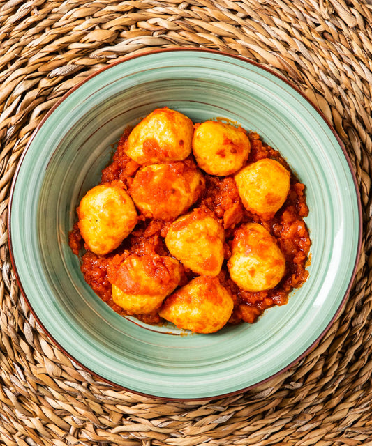 Ciotola verde chiaro in ceramica con bordo marrone contenente gnocchi di patate ripieni di salsiccia in sugo al pomodoro per un pasto completo dal gusto tradizionale