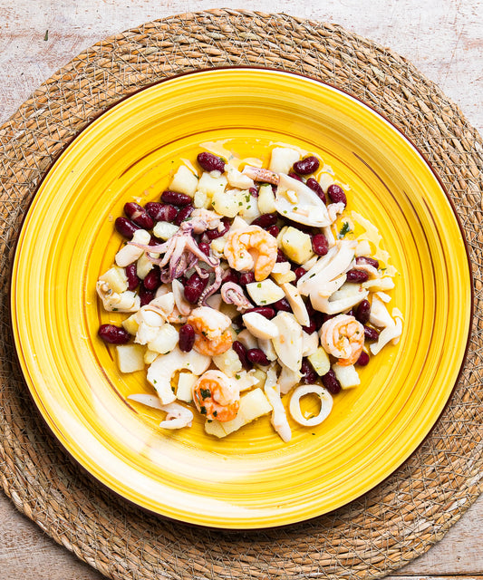 Vibrante piatto giallo in ceramica con insalata di calamari gamberi fagioli e patate colorata