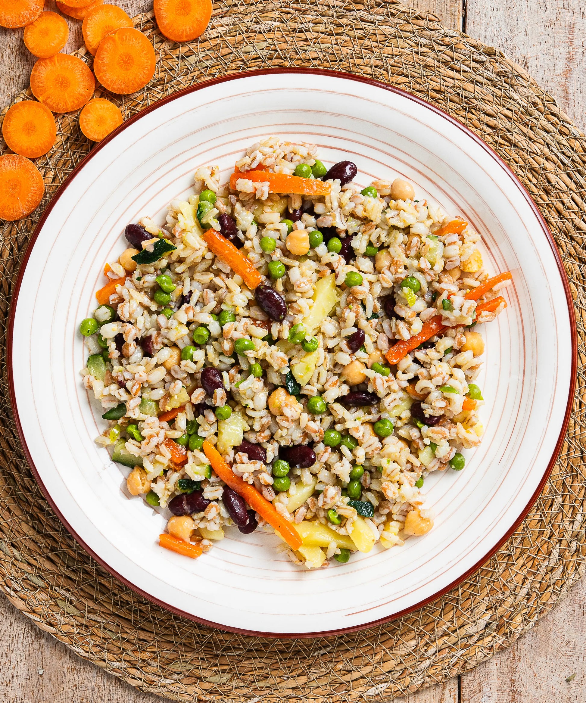 Insalata di cereali e legumi con zucchine e carote in ciotola bianca con bordino marrone ricca di proteine e cereali colorati