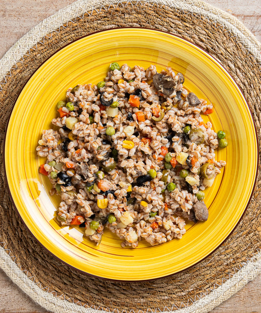 Insalata di farro con tonno funghi olive e mais servita su un piatto ceramico giallo vibrante con sottopiatto intrecciato