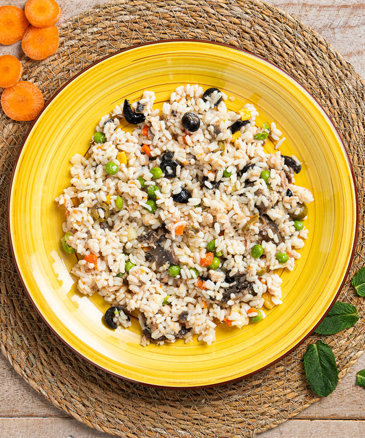 Una vivace insalata di riso classica con riso integrale, piselli verdi, carote e olive scure su piatto giallo ceramico