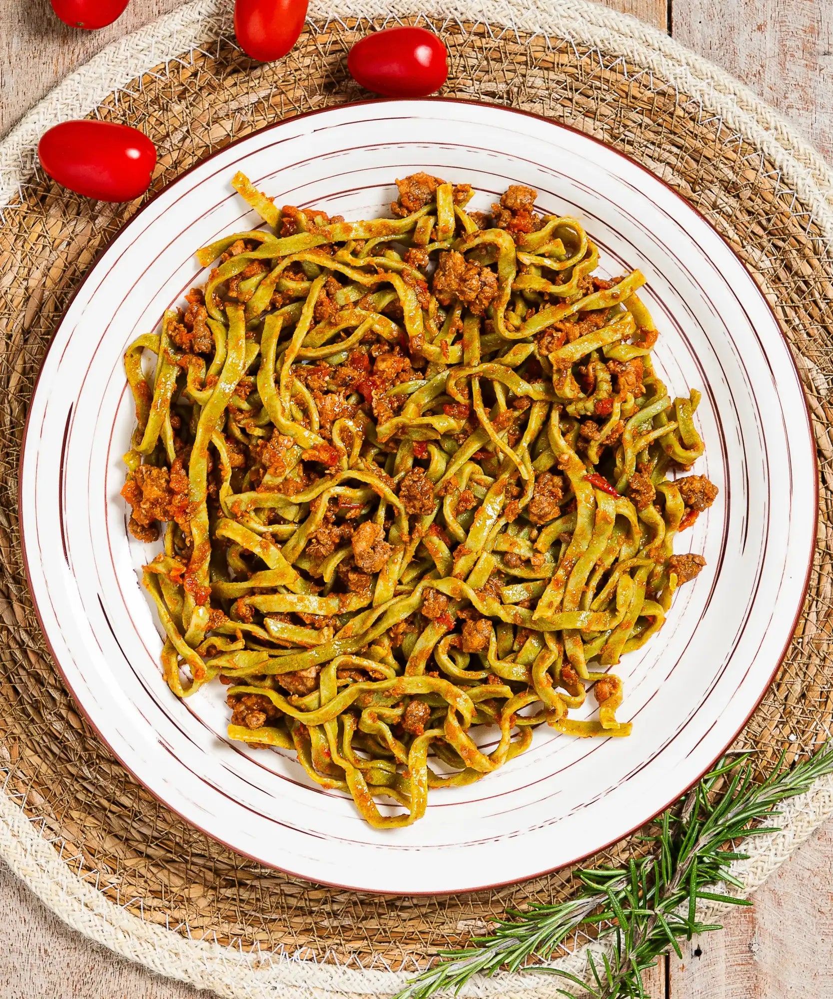 Un piatto di fettuccine verdi vivaci con un ricco sugo di carne, servito su un piatto di ceramica bianco con sottili anelli concentrici brunastri.