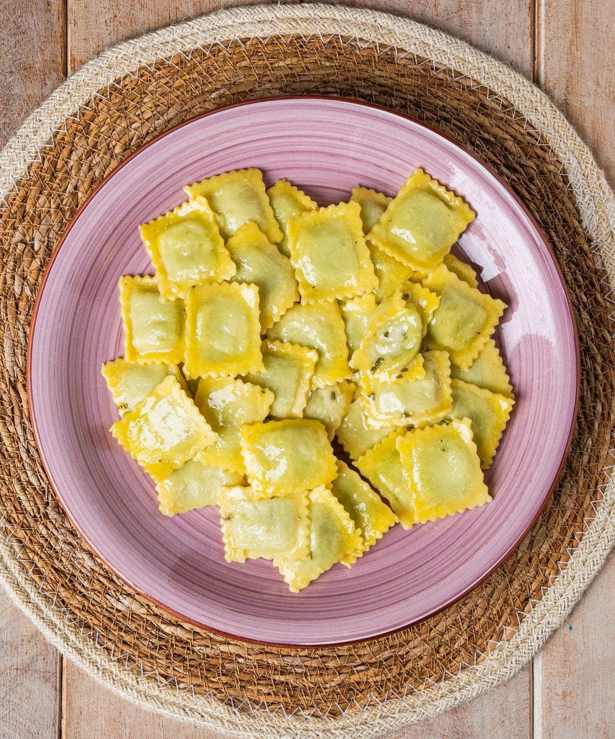 Una porzione di ravioli burro e salvia verdi e gialli su un piatto rosa in ceramica con grana padano dop