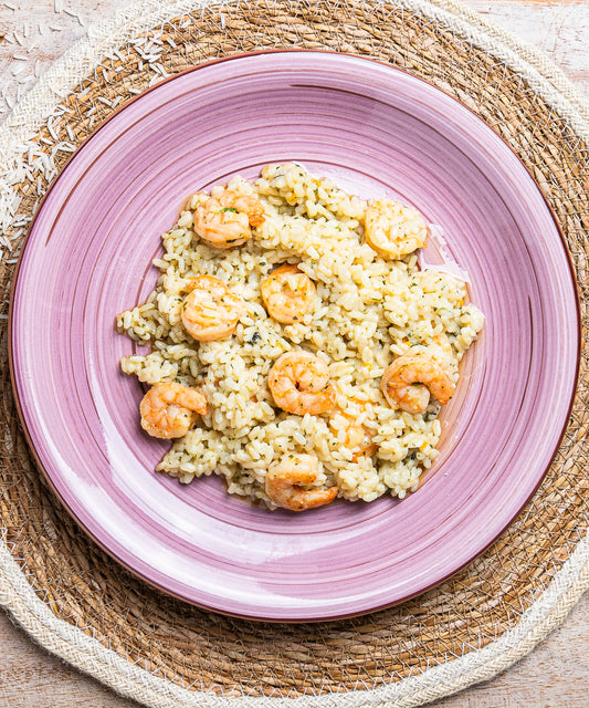 Risotto al mojito con gamberi e zucchine servito su un piatto di ceramica rosa con scanalature concentriche