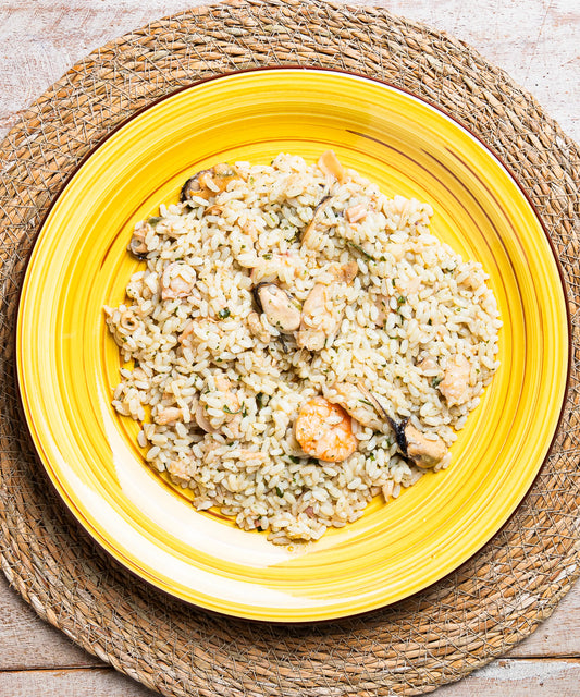 Risotto con frutti di mare servito su un piatto ceramico giallo vibrante con scanalature concentriche
