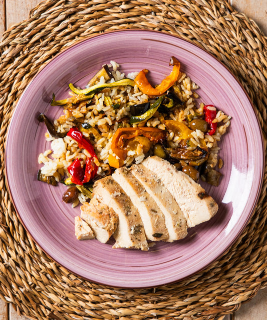 Piatto in ceramica lavanda con tagliata di pollo, riso carnaroli, verdure colorate e olive taggiasche per un pasto sano