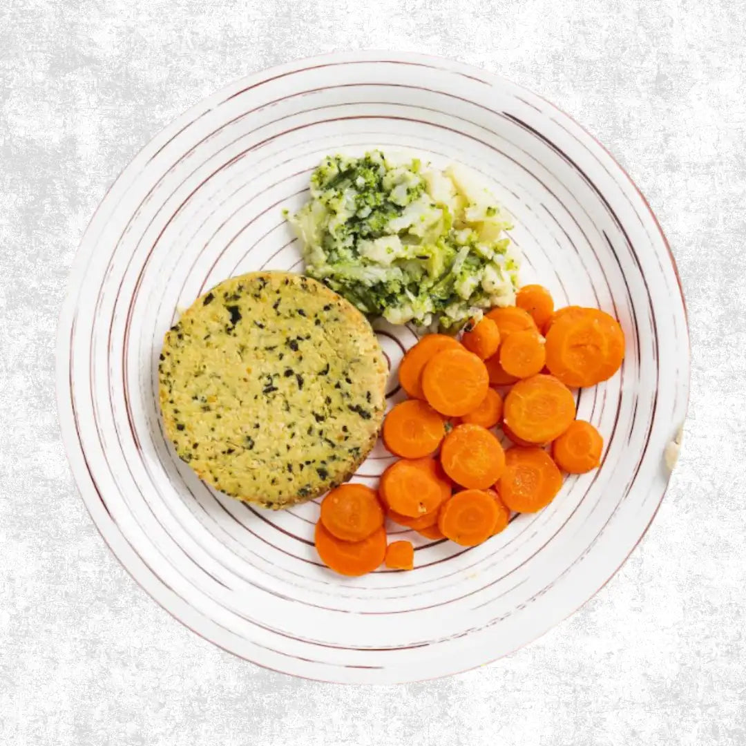 Un tortino vegetale rotondo e verdastro-giallastro, con scaglie verdi scure, è appoggiato su un piatto bianco con strisce marroni concentriche.