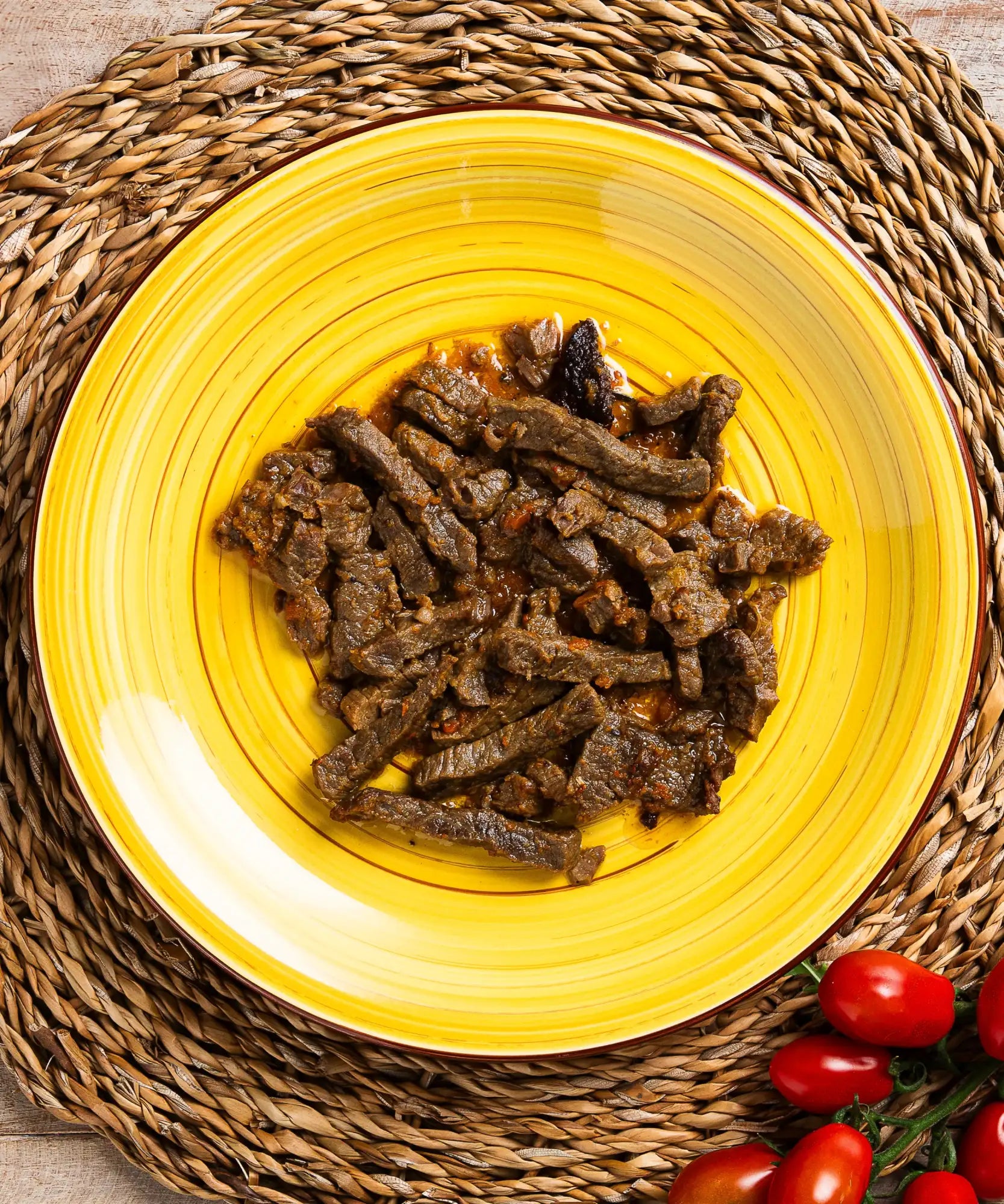 Un vivace piatto di ceramica giallo con motivi a rilievi concentrici ospita un piatto di manzo affettato scuro e saporito.